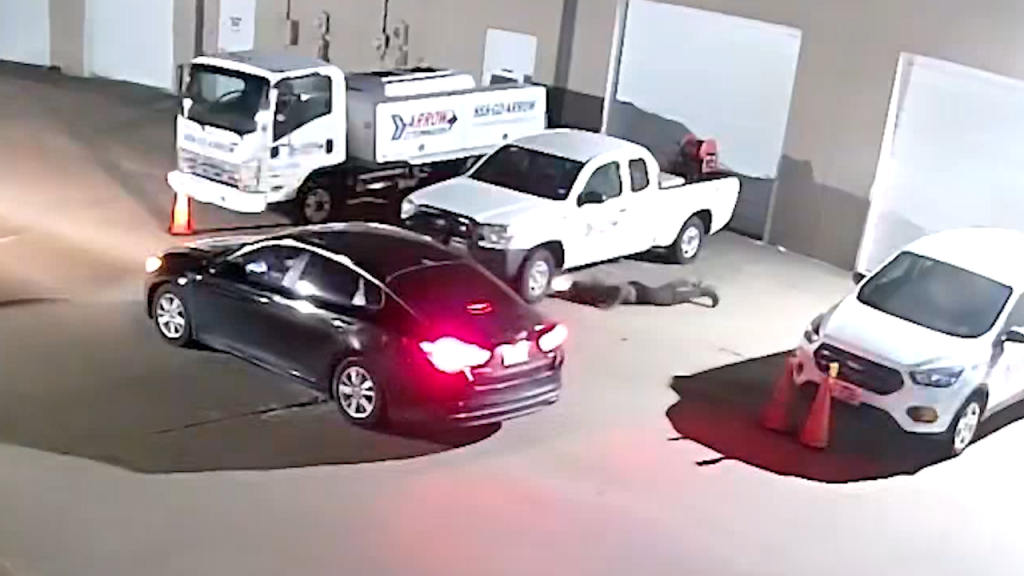 thief looks for catalytic converter under white truck